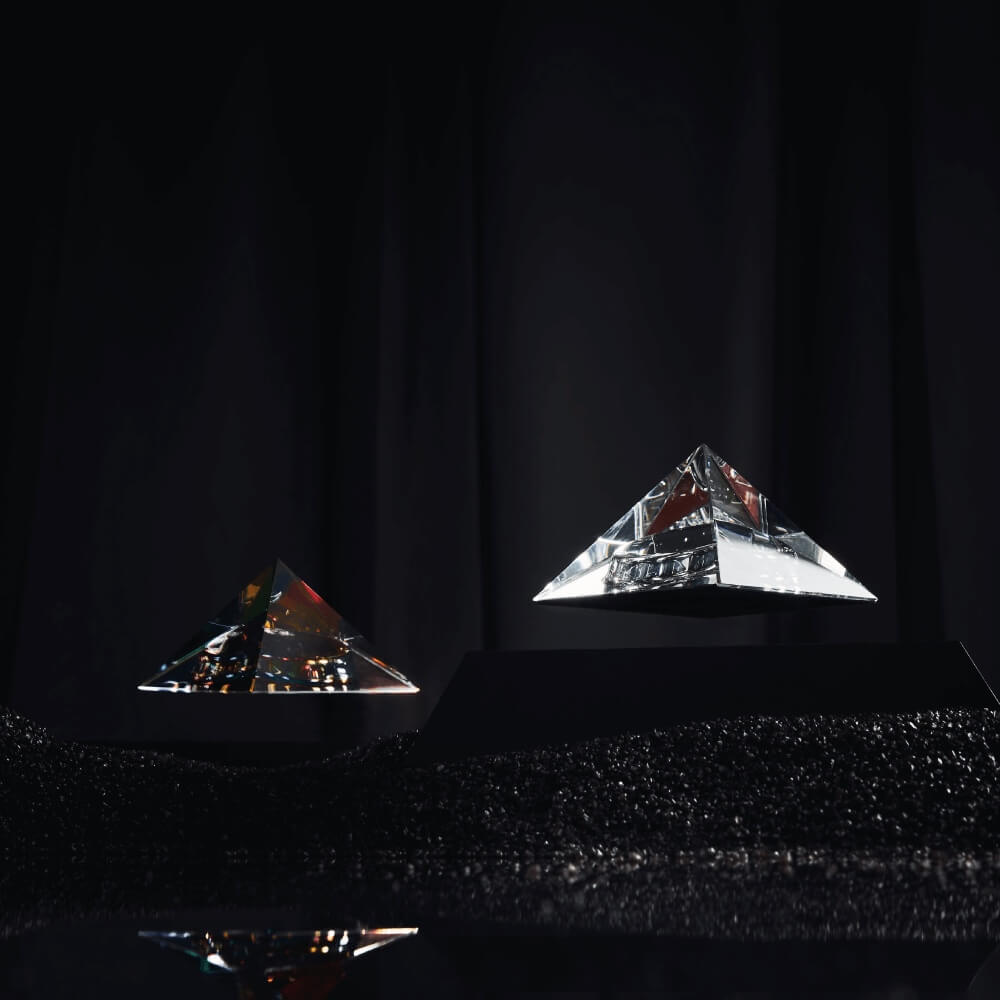 2 levitating pyramids Py by Flyte, clear and iridescent crystal tops with black bases in a dark interior setting
