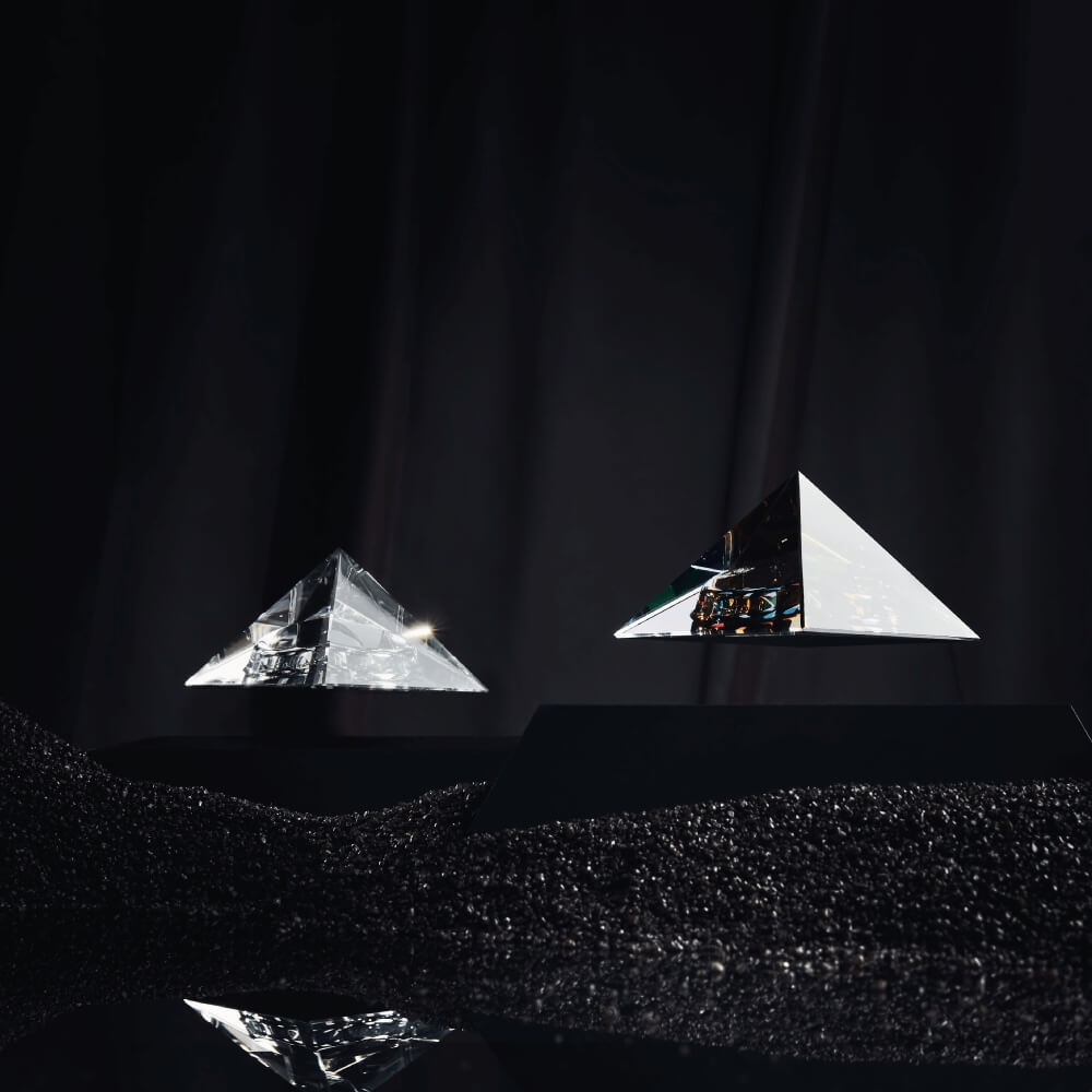 2 levitating pyramids Py by Flyte, iridescent and clear tops with black bases in a dark mysterious setting