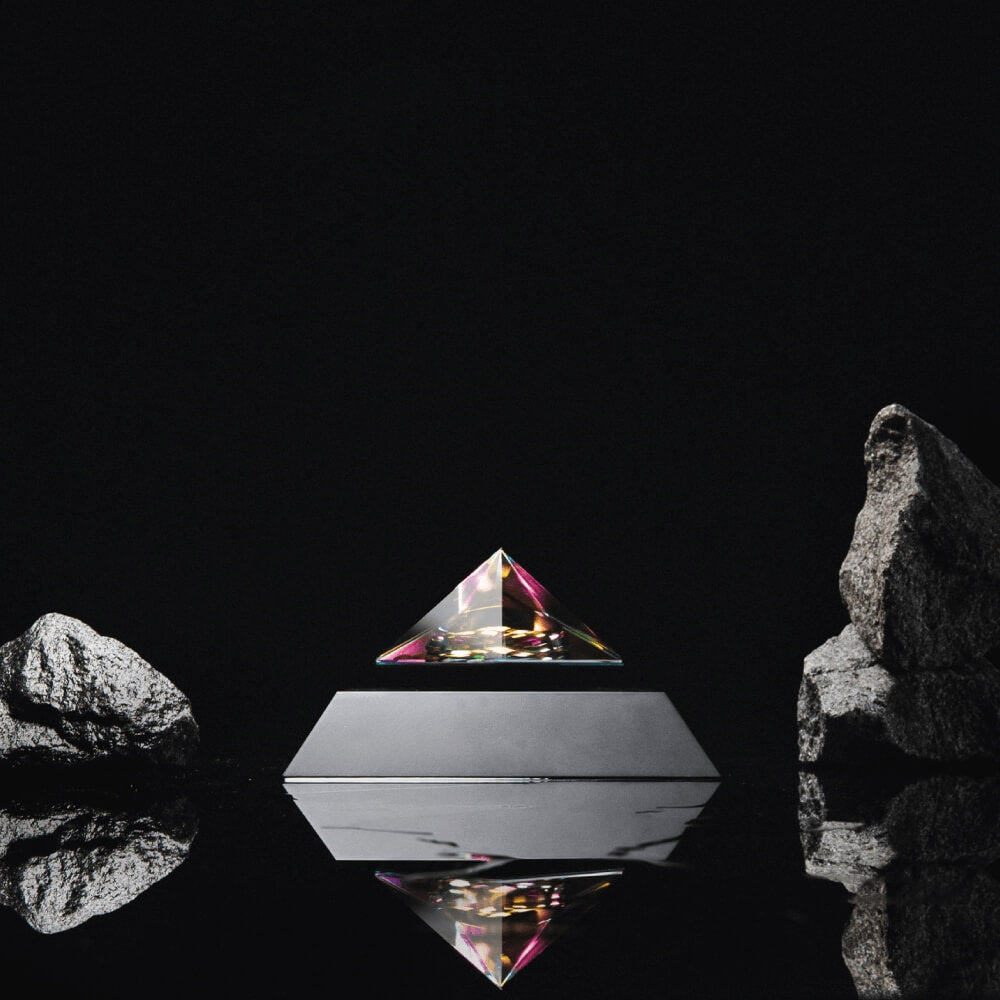 Levitating pyramid Py by Flyte, iridescent crystal top, black base option in a dark setting surrounded with rocks