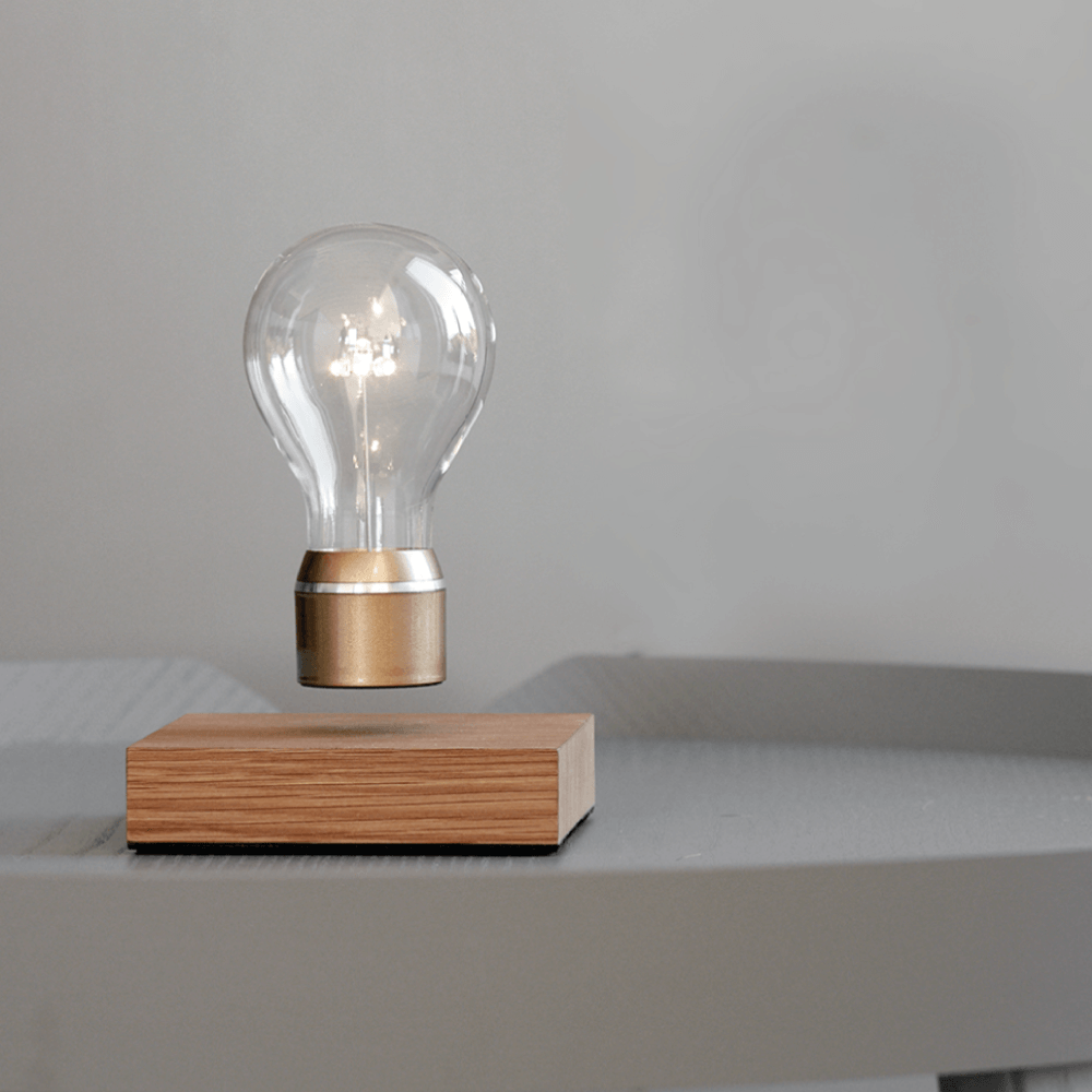 Levitating light bulb Light by Flyte, oak wood base with gold cap bulb in a light interior setting