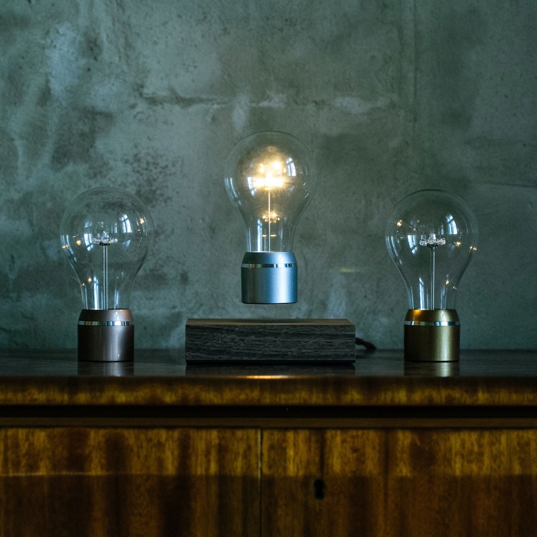 Levitating light bulb Light Edison by Flyte, chrome cap bulb with walnut magnetic base, placed on a table showing 2 alternative version of the Edison collection bulbs - gold and copper cap bulbs.