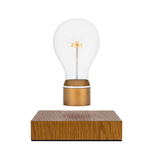 Product photo of levitating light bulb, oak wood magnetic base with gold cap bulb on a white background