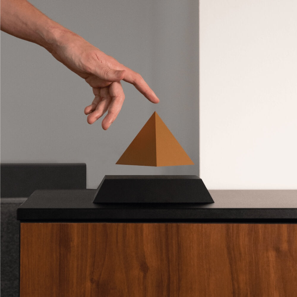 Levitating pyramid Py by Flyte, gold top on a black base version, lifestyle photo with a hand pointing to the pyramid top