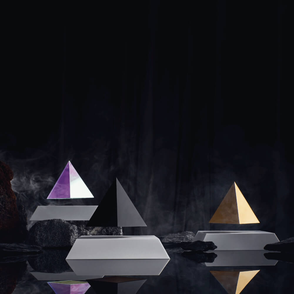 3 levitating pyramids Py by Flyte, iridescent, black, gold tops on white bases, lifestyle photo in a dark, mysterious setting