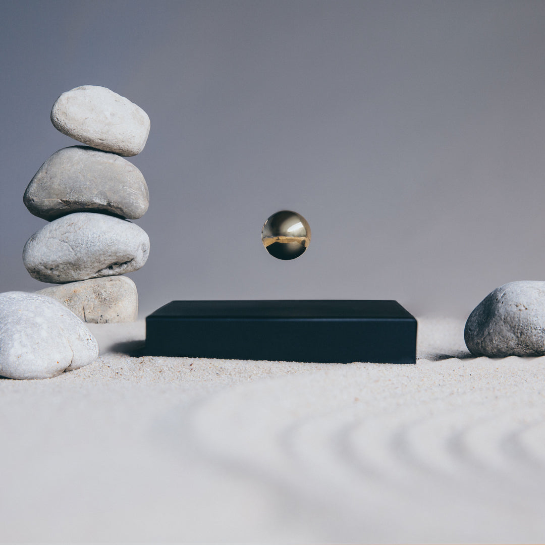 Levitating sphere Buda Ball by Flyte, gold sphere, black base option in a Zen garden setting with rocks and sand