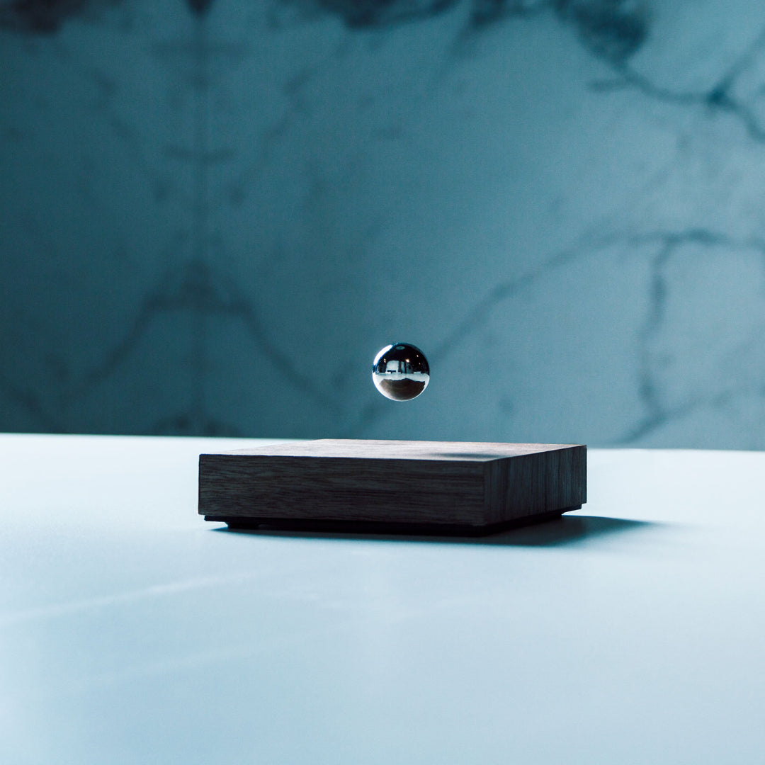 Levitating sphere Buda Ball by Flyte, chrome sphere, walnut base version placed on a table, front view